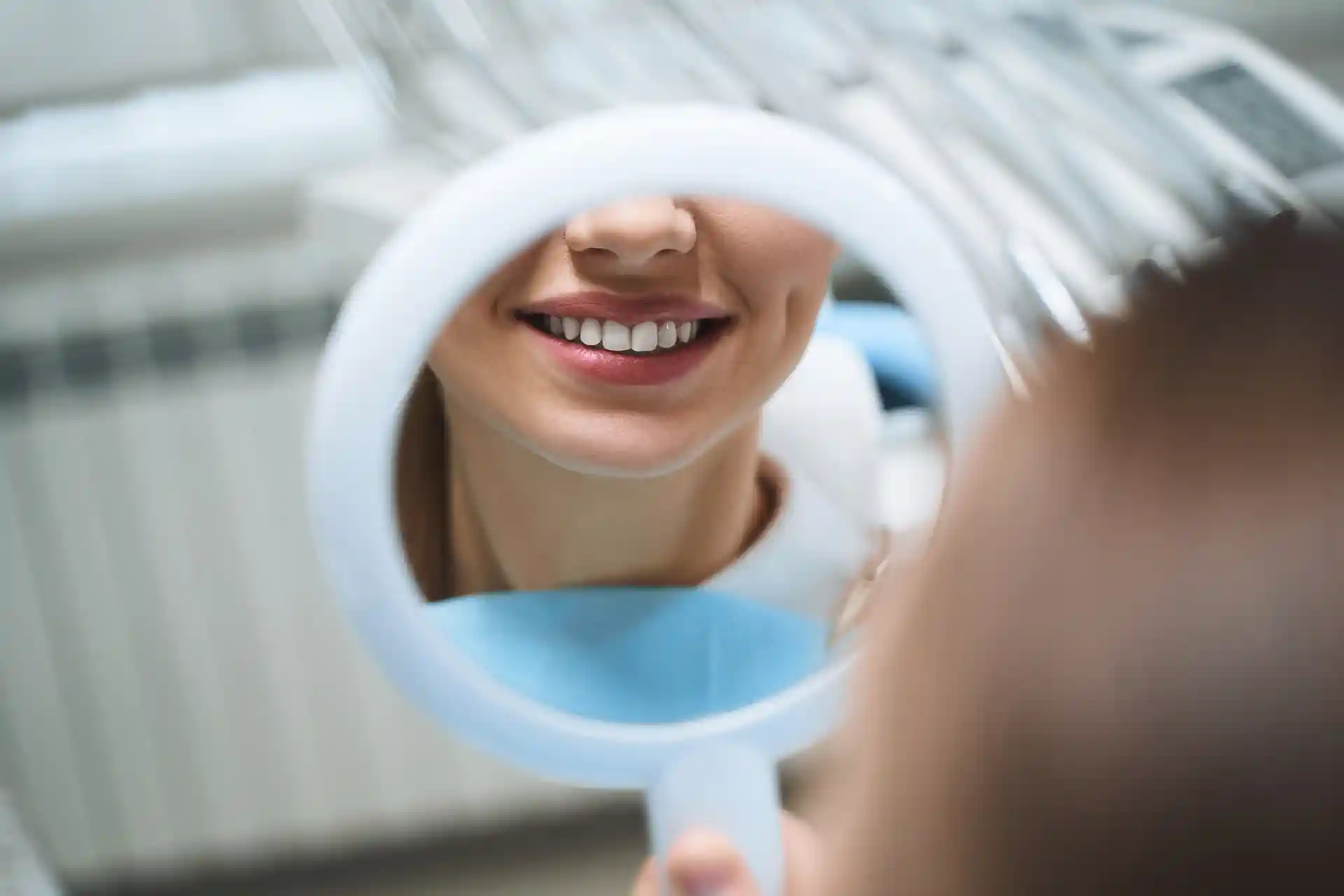 woman smiling in dental mirror after teeth whitening